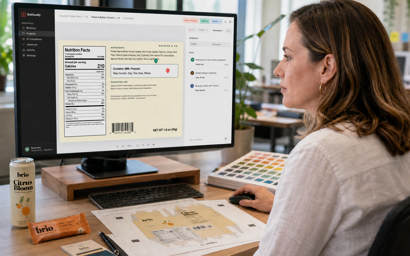 Packaging specialist reviewing Citrus Bloom artwork in GoVisually with a can, printed dieline and colour samples on her desk